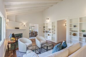 A spacious living room with a fireplace, white sofas, a glass coffee table, and a bookshelf. - 3833 Treetops - Updated, Custom Home in the Trees (Carmel)