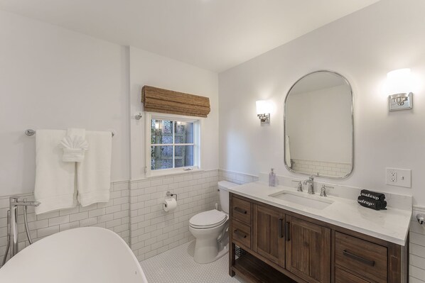 A bathroom with a toilet, sink, and bathtub. There is a window with a view of trees, a towel rack with towels, and a mirror above the sink. - 3833 Treetops - Updated, Custom Home in the Trees (Carmel)