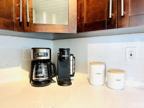 Eine Küche mit Holzausstattung, einer Kaffeemaschine, einer Keurig-Kaffeemaschine sowie zwei Behältern, beschriftet mit 'Kaffee' und 'Zucker'.