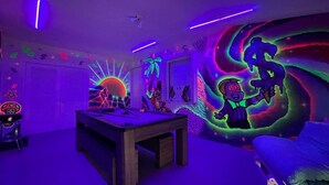 Una habitación con una pared iluminada con neón, una cama, un escritorio y una silla.