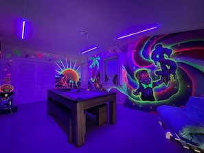 A room with a neon-lit wall, a bed, a desk, and a chair.