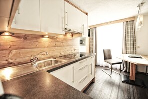 A modern kitchen with white cabinets, a wooden backsplash, stainless steel appliances, and a dining area with a table and chairs. - HIRSCH by Summit Residence (Serfaus)