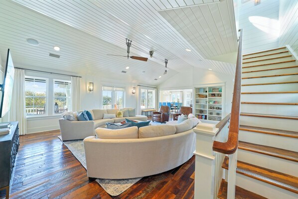 A spacious living room with a large sectional sofa, a wooden staircase, and a view of the outdoors.