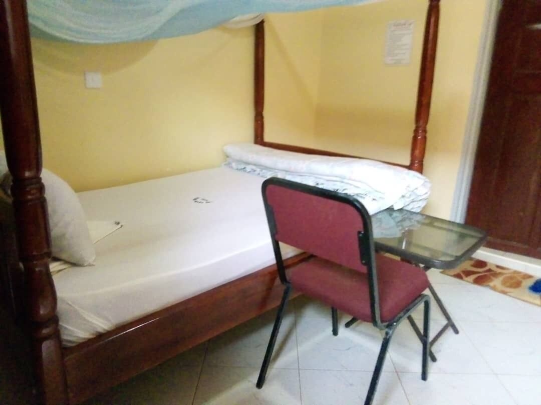 A single bed with a wooden frame and a metal headboard, a red upholstered chair, and a small glass table.