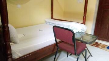 Una cama individual con estructura de madera y cabecera de metal, una silla tapizada de color rojo y una pequeña mesa de vidrio.