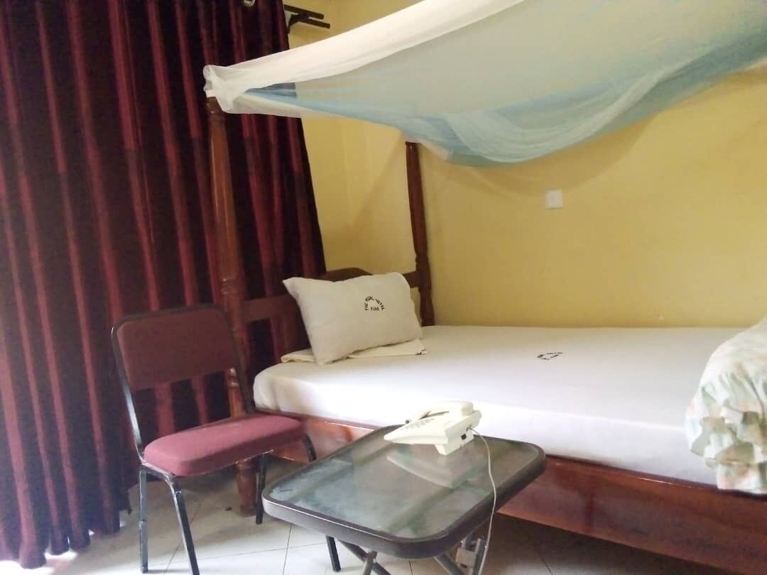 A single bed with a canopy, a chair, and a small table with a phone.