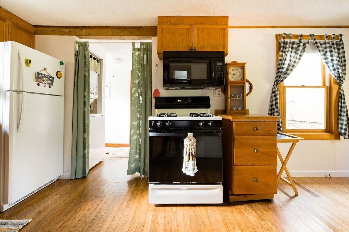 A compact kitchen with a white refrigerator, a black microwave, a stove, and wooden cabinets.