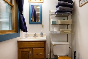 Ein Badezimmer mit einem Holzkorpus, einem weißen Waschbecken, einem Spiegel und einem Metallregal mit Handtüchern.