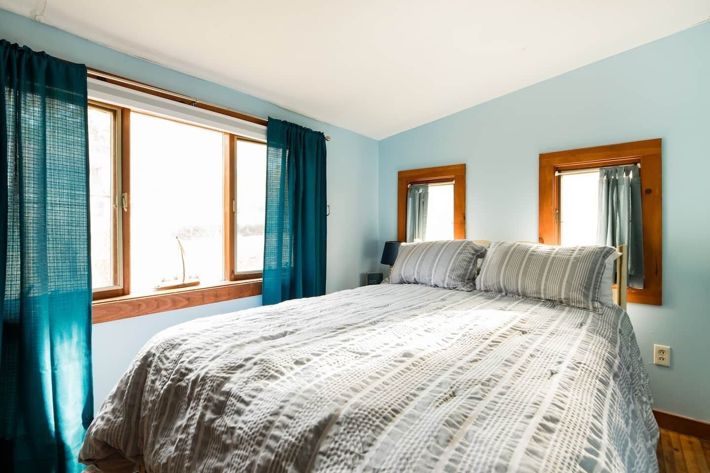 Une chambre avec un grand lit, deux fenêtres avec des rideaux et une vue sur l’extérieur.