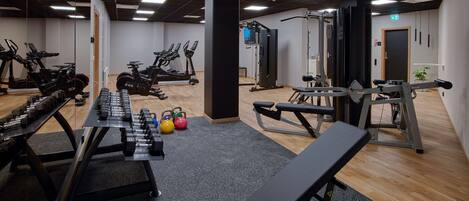 Un gimnasio con equipo de ejercicio, una banca y un espejo.