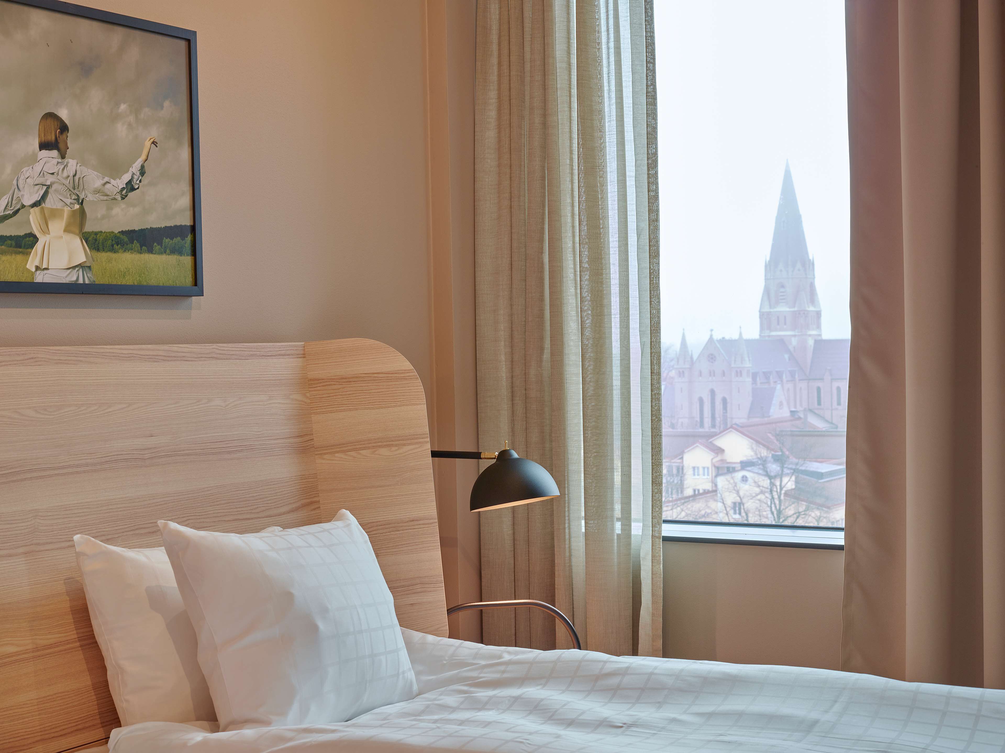Una habitación de hotel con cama, mesita de noche, lámpara y un cuadro en la pared.