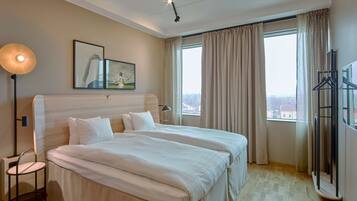 Ein Hotelzimmer mit einem großen Bett, einem Nachttisch, einer Stehlampe, einem Bild an der Wand und Blick auf die Stadt durch das Fenster.