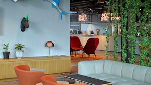 A modern interior with a reception desk, seating area, and decorative elements like a shark sculpture and hanging plants. - Scandic Örebro Central (Örebro)
