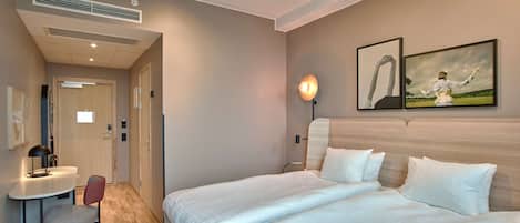Habitación de hotel con una cama, un escritorio y una silla. Hay una lámpara en el escritorio y un cuadro en la pared.
