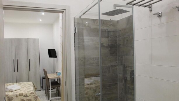 A hotel room with a bed, a desk, a chair, a wardrobe, and a glass-enclosed shower area. - Double room in the center of Catania (Catania)