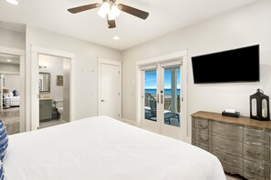 A bedroom with a bed, a television, a dresser, and a balcony with a view of the ocean.