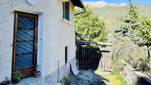 Una casa rústica con puerta de madera, una ventana pequeña y una planta en maceta en el porche.