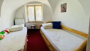 Una habitación pequeña y acogedora con dos camas individuales, una mesita y una ventana con cortinas.