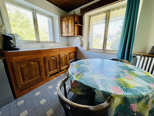 Una cocina con armarios de madera, una mesa con mantel floral y una ventana con cortinas.