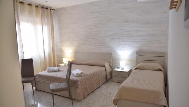 A hotel room with two beds, a chair, a desk, and a nightstand with a lamp. - Triple room in the center of Catania (Catania)