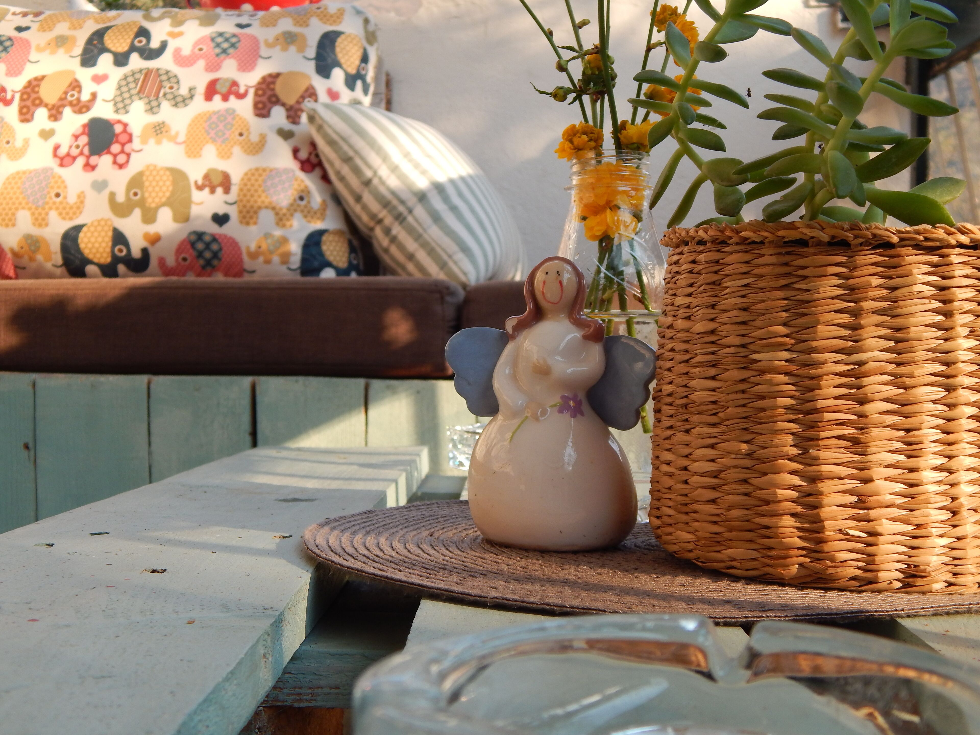 Un cesto in vimini con una statuina di angelo in ceramica e fiori gialli su un tavolo di legno.