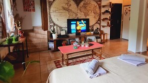 A cozy living room with a large world map mural, a television, a coffee table with decorative items, and a bed with towels. - Impeccable Apartment With View in Dolna Matka (Matka)