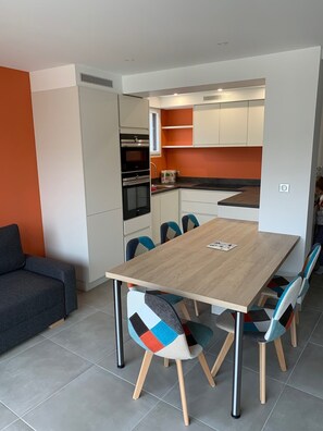 A modern kitchen with white cabinets, a wooden dining table, and colorful chairs. - LE CLOS DES 2 CAPS - RENOVATED CONTEMPORARY 2 BED APARTMENT 2 STEPS FROM THE SEA (Wimereux)