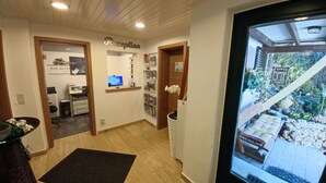 A reception area with a reception desk, a computer, and a wall-mounted shelf with brochures. There is a small potted plant and a black mat on the floor. - Apartments Zur alten Post (Willingen)