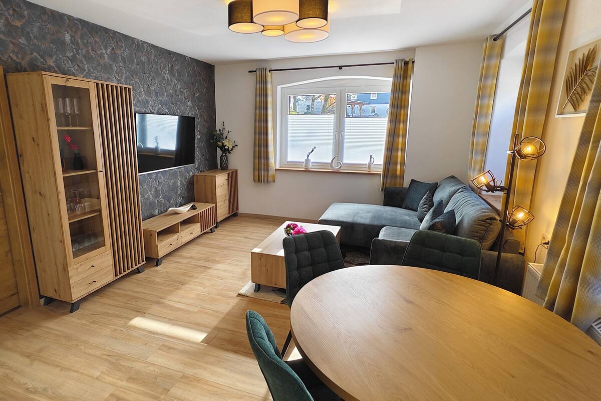 A modern living room with a wooden floor, a sofa, a TV, and a dining table.