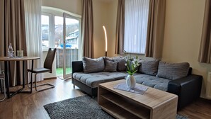 A modern living room with a grey sofa, a wooden coffee table, and a dining area with a table and chairs. - Apartments Zur alten Post (Willingen)
