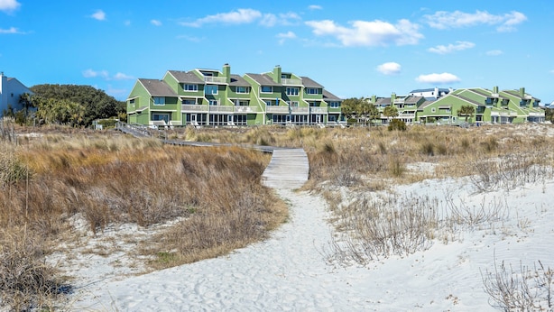 Een hotel aan het strand, met een zandpad dat naar de ingang leidt.
