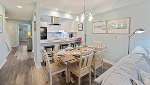 Een moderne keuken met witte kasten, een eethoek met houten stoelen en een lichtblauwe wand.
