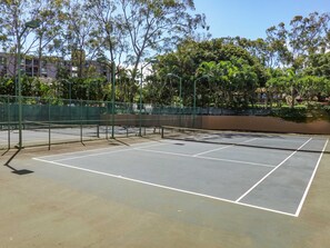 En utomhusbana för tennis, omgiven av träd och ett staket.