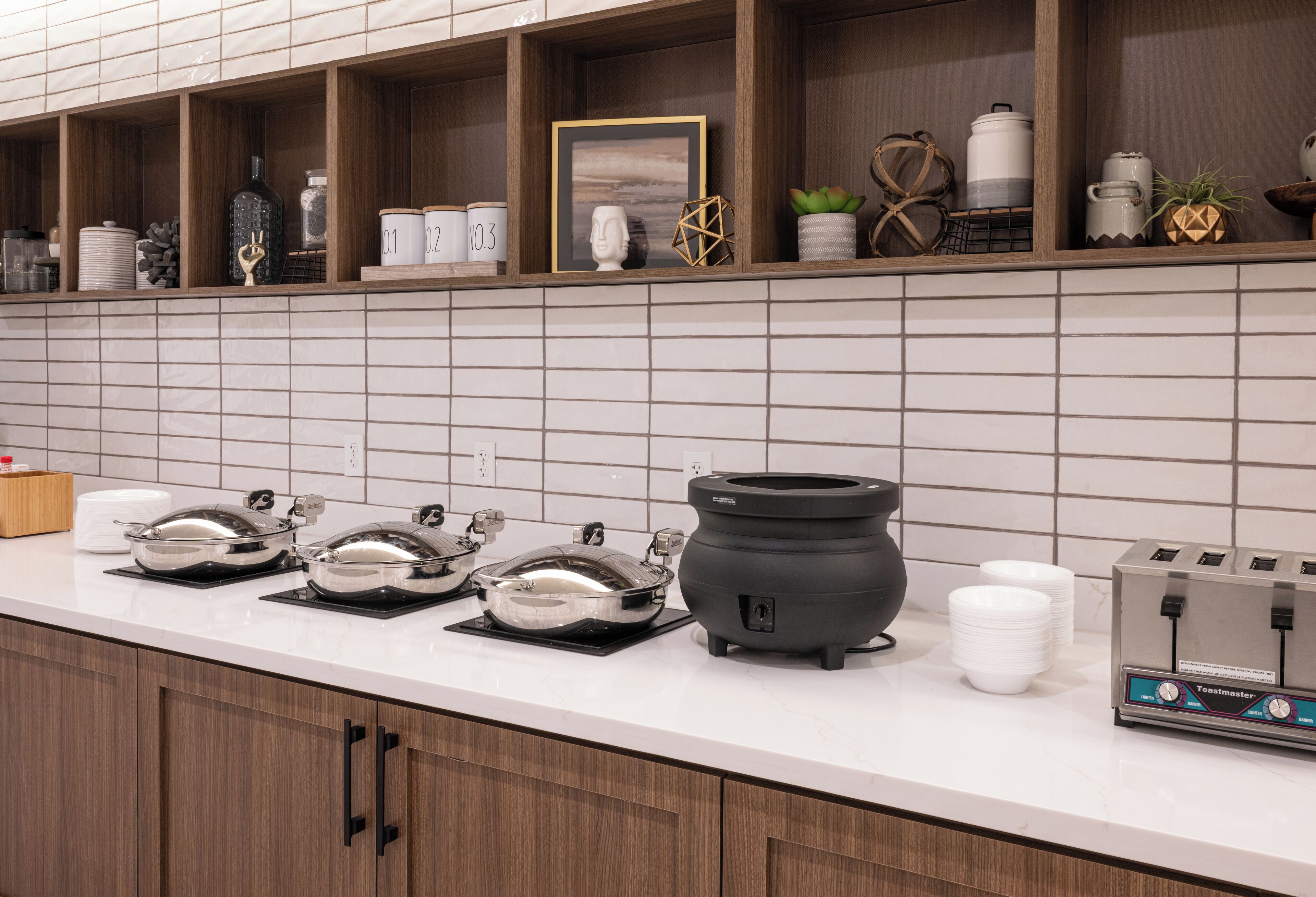A kitchen with a white countertop, wooden cabinets, and a toaster. There are several bowls and a pot on the counter.