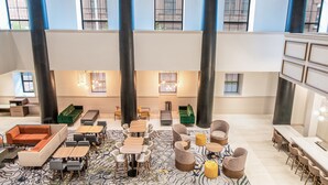 Eine großzügige Lobby mit hohen Decken, großen Fenstern und unterschiedlichen Sitzgelegenheiten, darunter Sofas, Sessel und Tische.