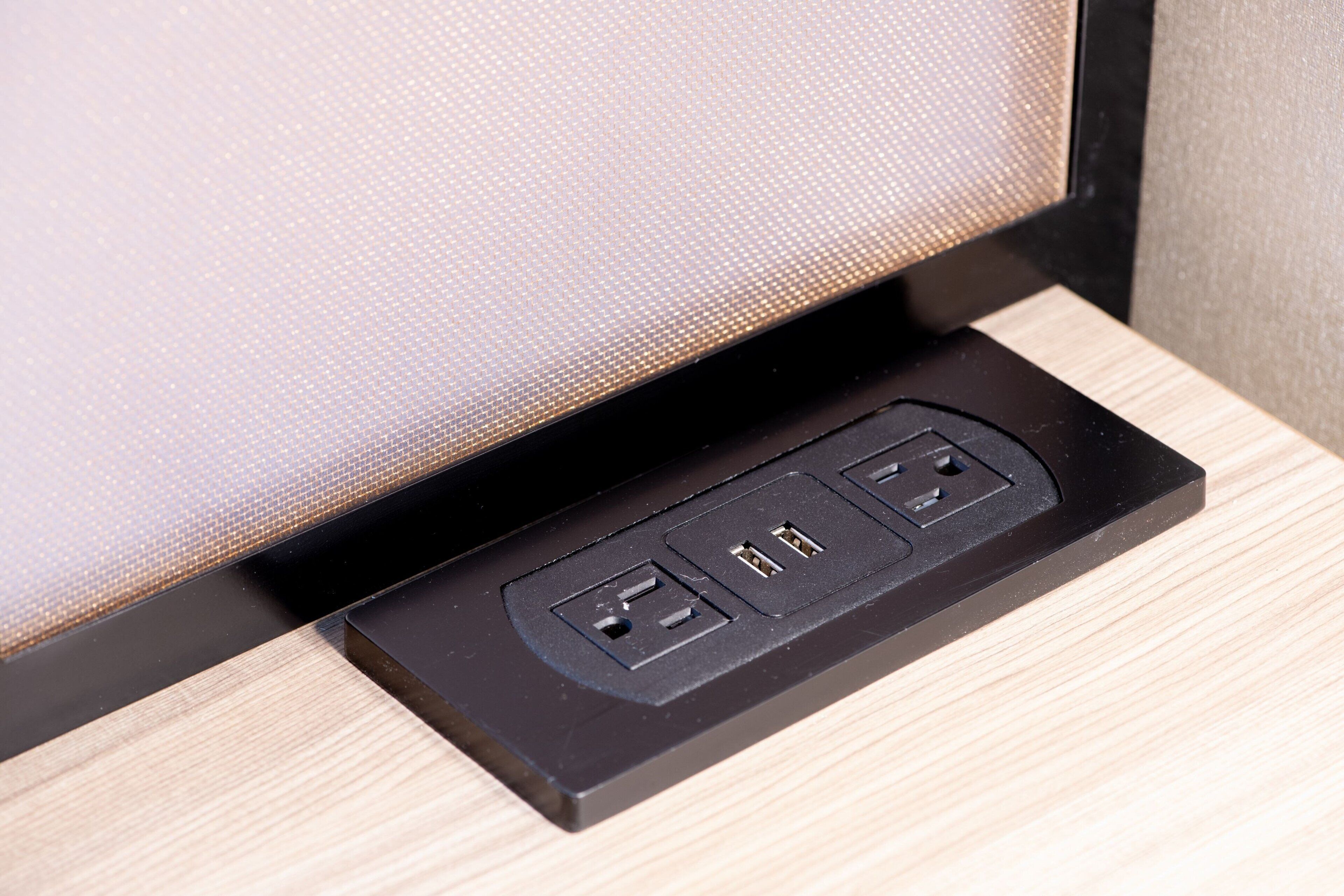 Una regleta negra con dos puertos USB y un enchufe estándar sobre una superficie de madera.