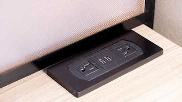Una regleta negra con dos puertos USB y un enchufe estándar sobre una superficie de madera.