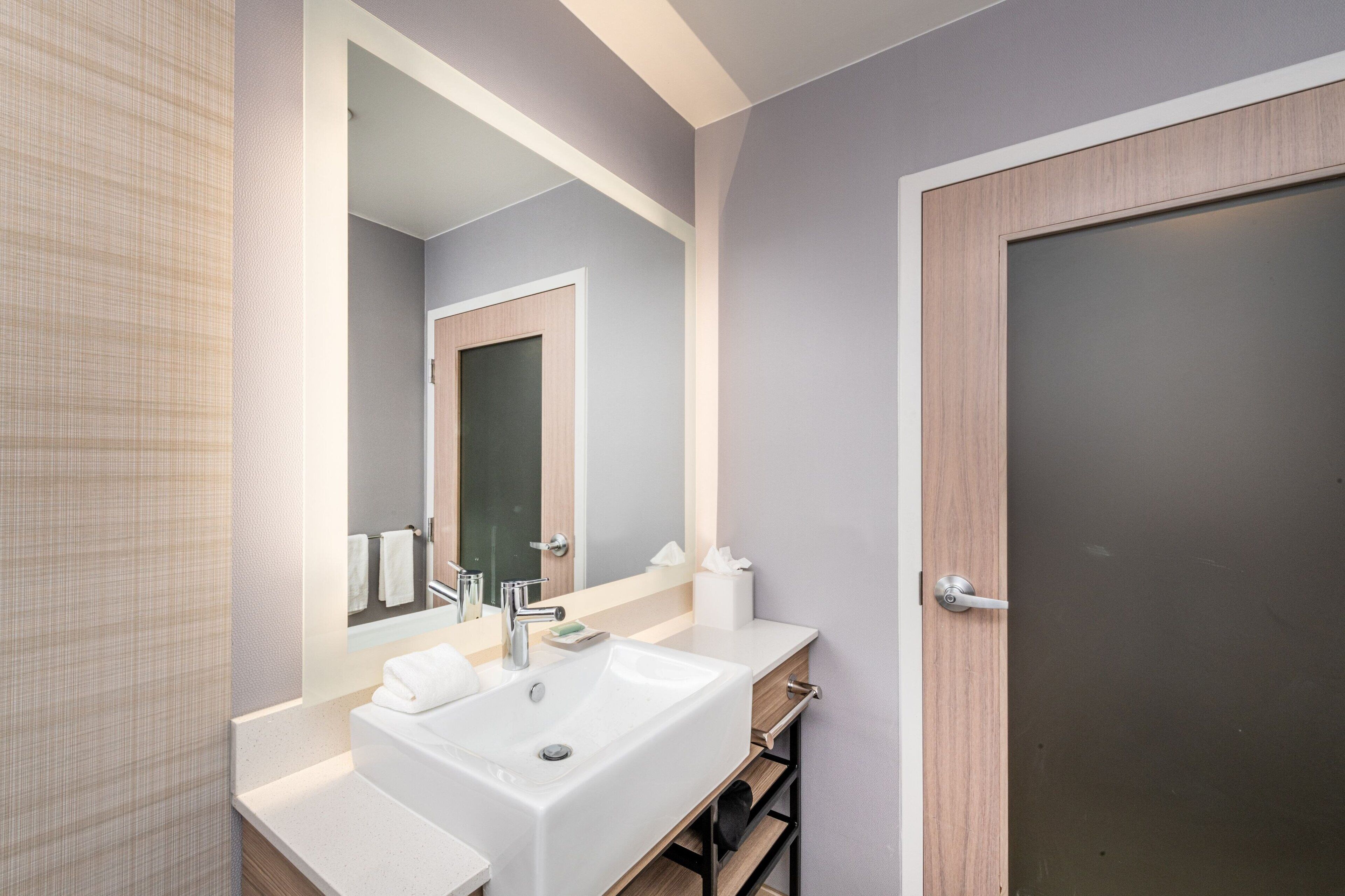 A modern bathroom with a white sink, a mirror, and a wooden door.
