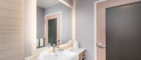 A modern bathroom with a white sink, a mirror, and a wooden door.