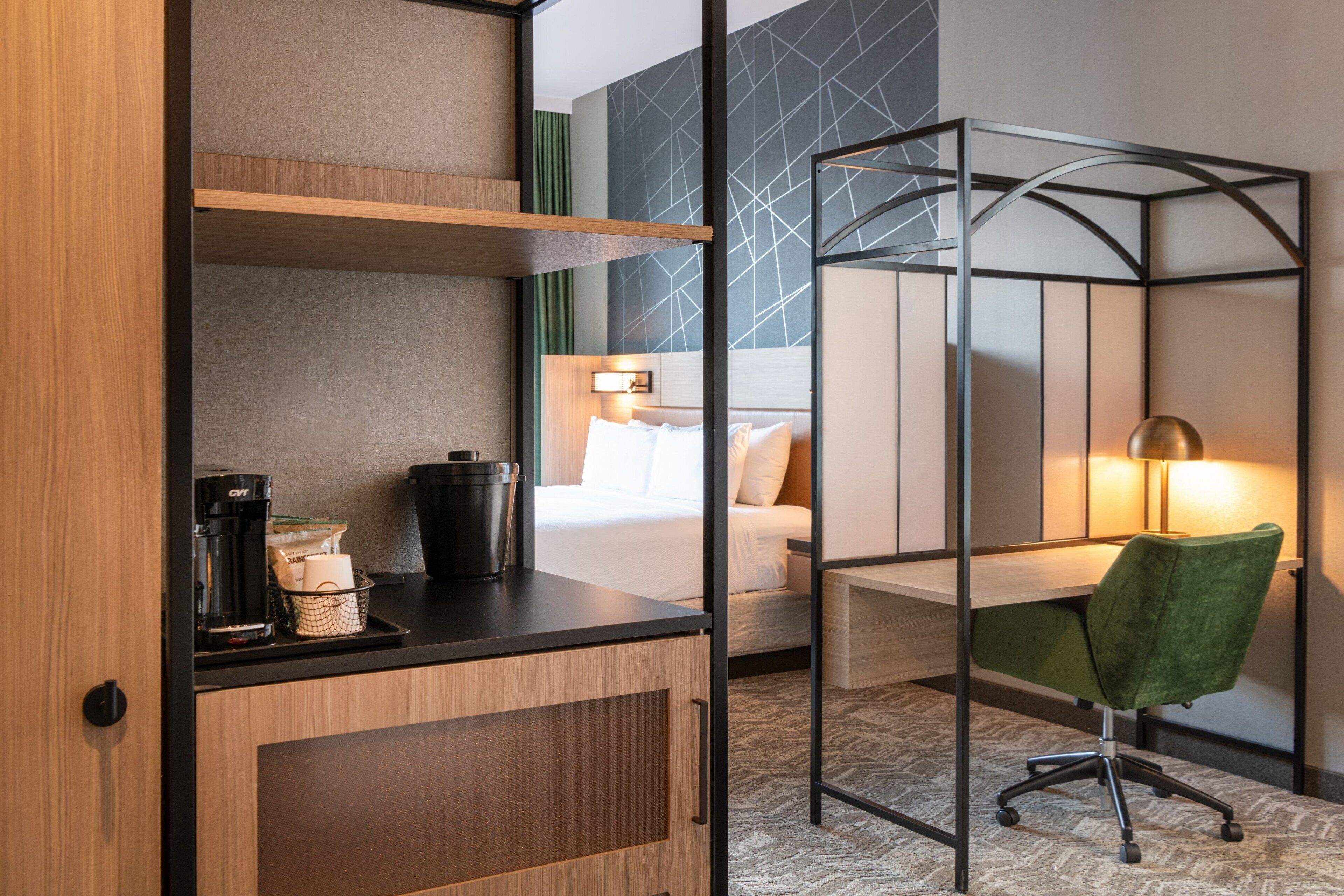 A hotel room with a bed, a desk, a chair, and a coffee maker.