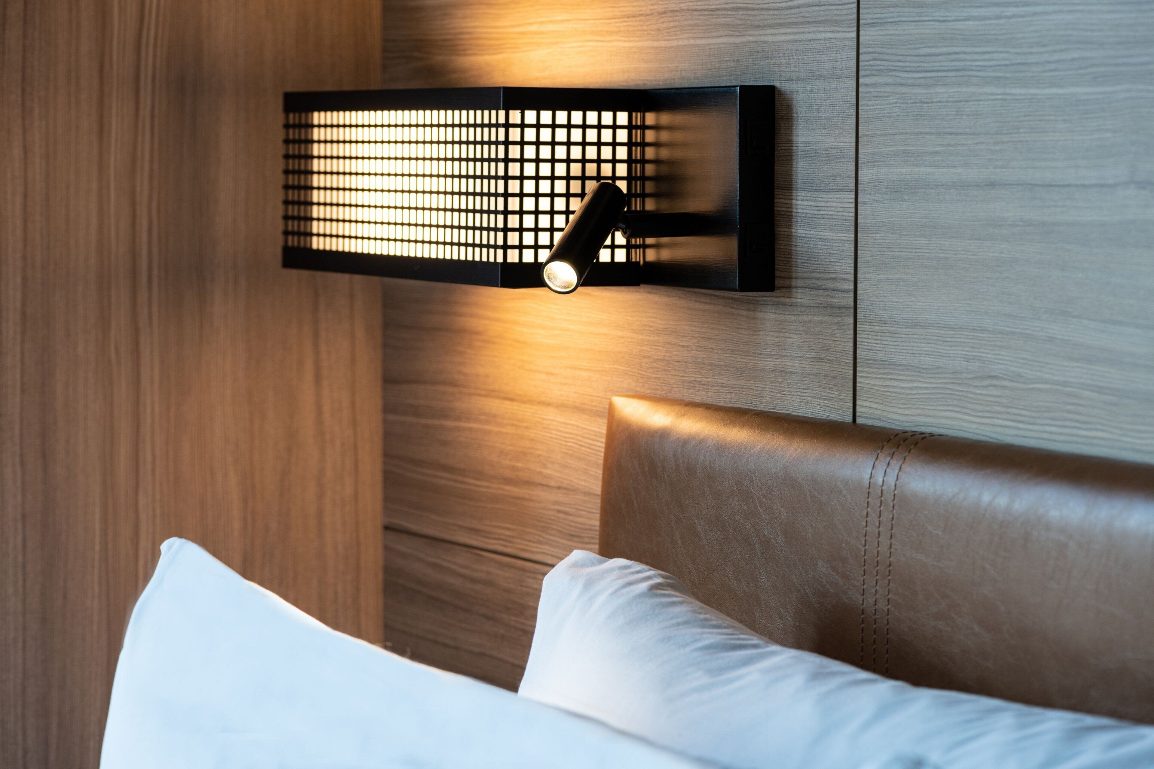 A modern bedroom with a wooden headboard, a wall-mounted light fixture, and a white pillow.