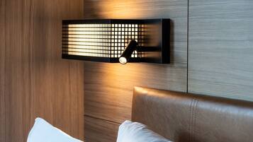 A modern bedroom with a wooden headboard, a wall-mounted light fixture, and a white pillow.
