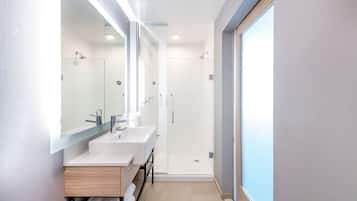 A modern bathroom with two sinks, a glass shower enclosure, and a large mirror.