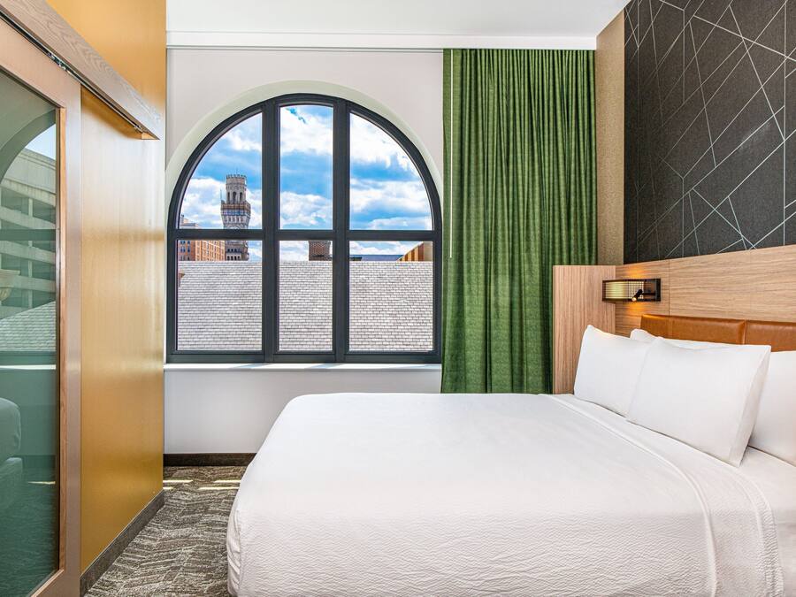 Ein Hotelzimmer mit einem großen Bett, einem Fenster mit Blick auf Gebäude, einem grünen Vorhang und einem modernen Wanddesign.