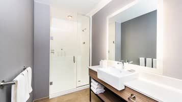 Un baño moderno con cabina de ducha de vidrio, un espejo grande y un mueble de tocador de madera con lavamanos blanco.