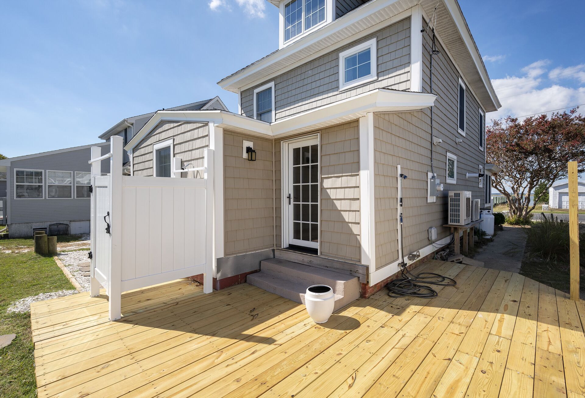 A two-story house with a wooden deck, a white front door, and a small porch area.