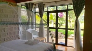 Ein Schlafzimmer mit Bett, Stuhl und Blick auf einen Garten durch eine Glastür.