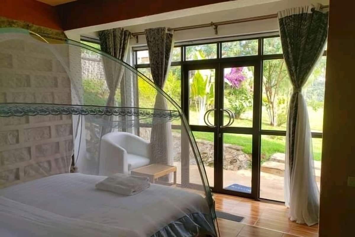A bedroom with a bed, a chair, and a view of the outdoors through a glass door.