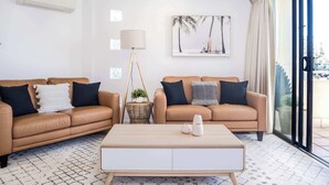 A living room with two brown leather sofas, a white coffee table, a floor lamp, and a large window with a view. - Tides & Tranquility - 2Bedroom Kings Beach Unit (Kings Beach)