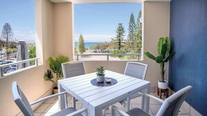 A balcony with a white table and chairs, potted plants, and a view of the sea. - Tides & Tranquility - 2Bedroom Kings Beach Unit (Kings Beach)